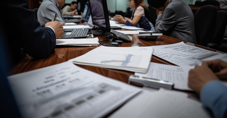 Photo of people working on a large table with lots of financial paperwork in front of them.