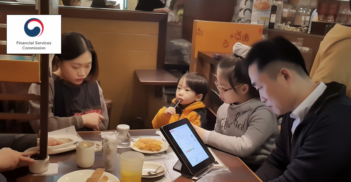 Photo of Korean family sitting at a restaurant with Father looking at tablet device.