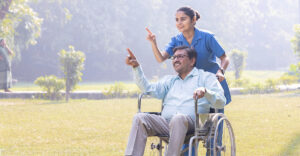 Photo of person in wheelchair being pushed by nurse in garden.