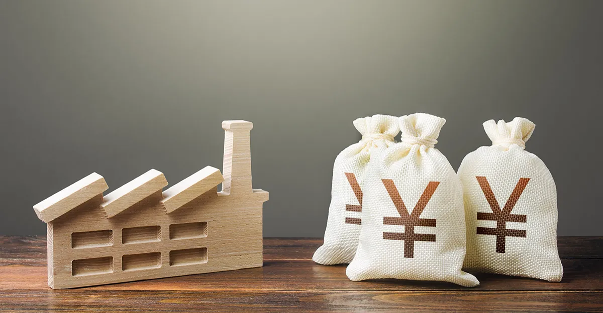 Photo of bags of Japanese yen next to a wooden representation of house/factory.