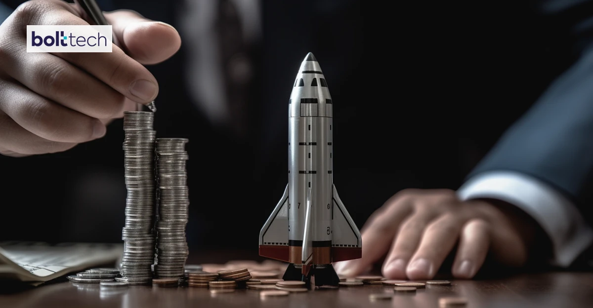 A photo of Space ship surrounded by coins and accountant holding pen. Bolttech logo in top left corner.