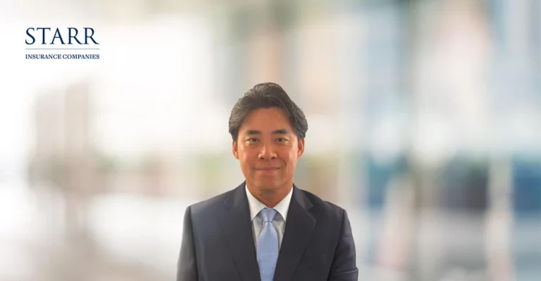 A man in a suit and tie is standing in front of a blurry background.