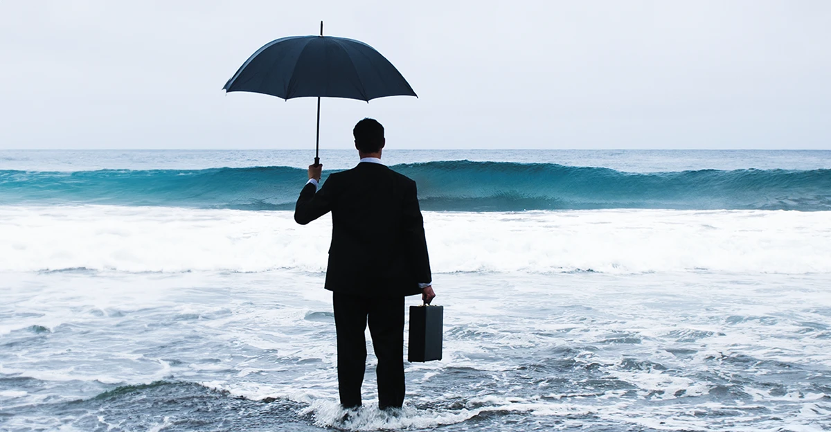 A businessman holding an umbrella in the ocean.