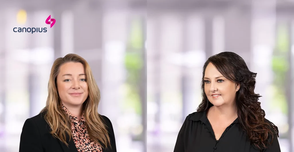 Two women standing next to each other in front of an abstract background.