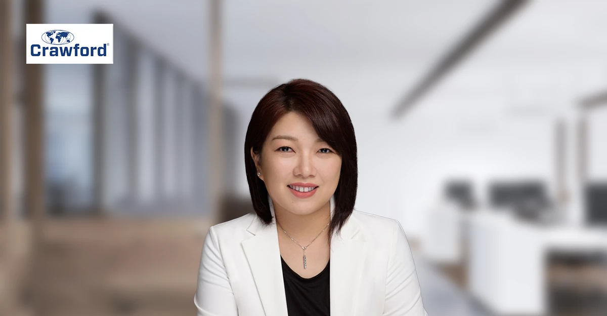 A woman in a white blazer is smiling in an office.