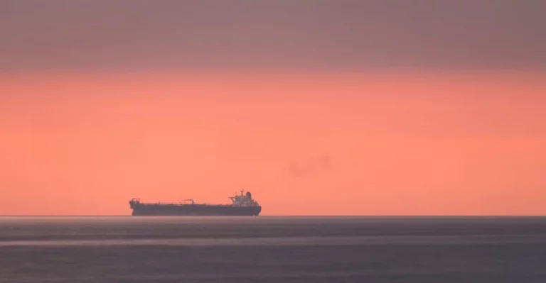 A large cargo ship in the ocean at sunset.