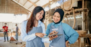 Two asian women using a tablet in a workshop.