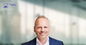 A man in a business suit smiling in front of a window.