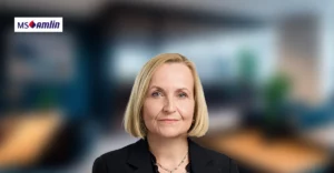 A woman in a business suit is standing in front of a blurry background.