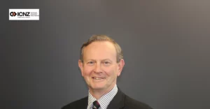 A man in a suit and tie smiling in front of a gray background.