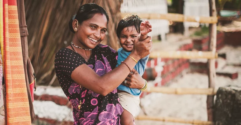 A woman holding a child in front of a house.