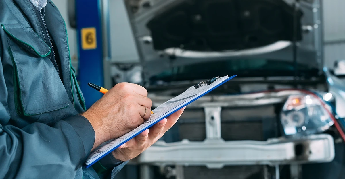 A mechanic is writing on a clipboard in front of a car.