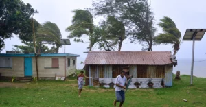 A group of people playing in front of a shack on the beach.