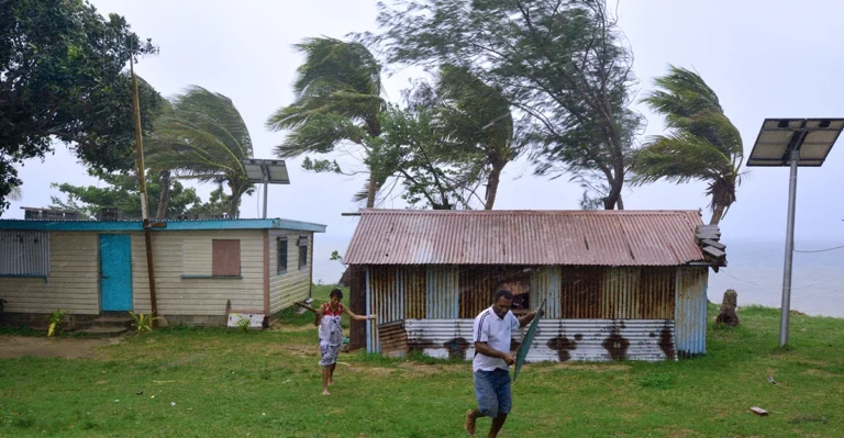 A group of people playing in front of a shack on the beach.