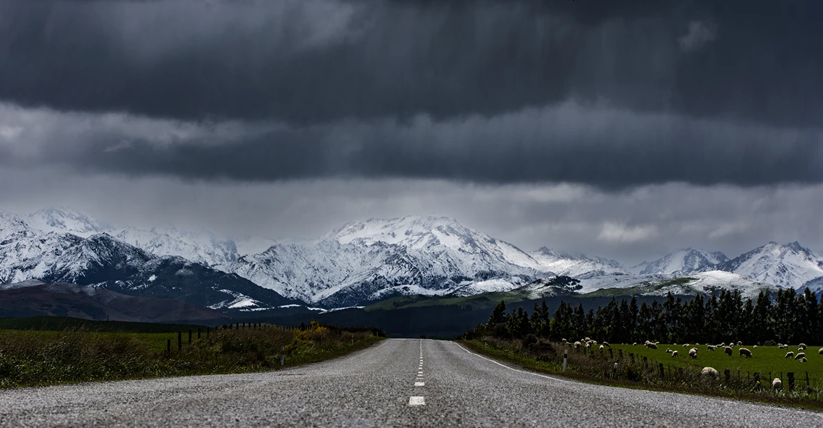 An empty road with snow capped mountains in the background.
