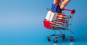 A hand is holding a shopping cart full of gifts.