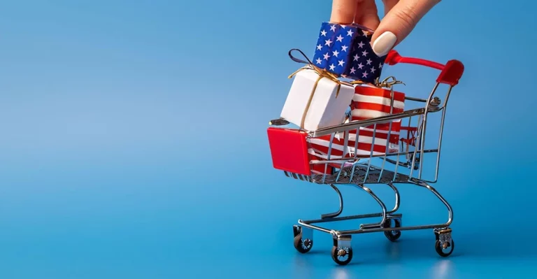 A hand is holding a shopping cart full of gifts.