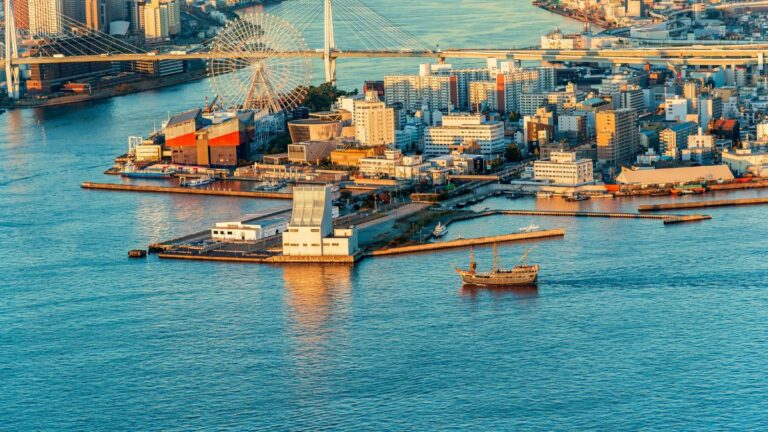 Aerial view of a coastal city with a large Ferris wheel, a bridge, and a busy waterfront.