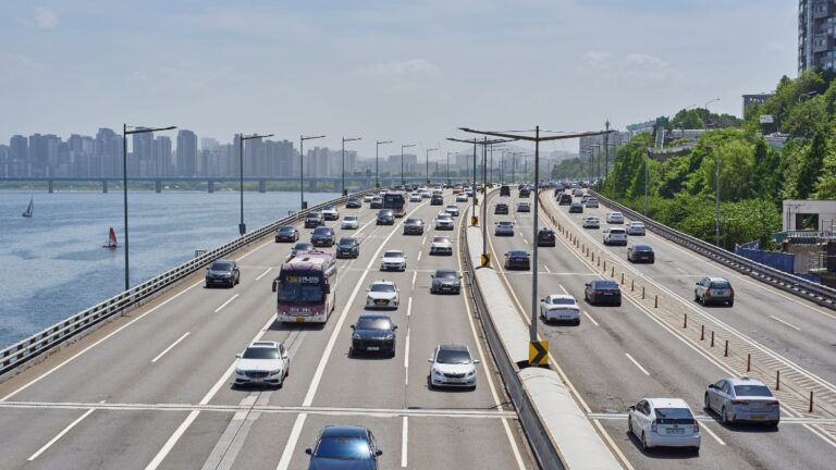 Busy multi-lane bridge highway over a body of water with a distant city skyline on the horizon