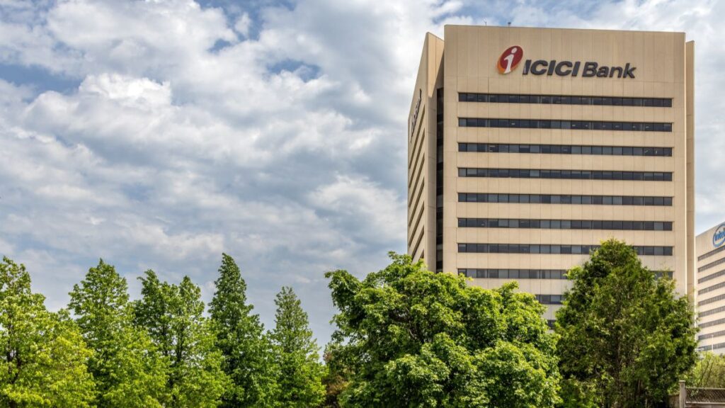 Tall beige ICICI Bank office tower with a red logo, framed by green trees under a cloudy sky.