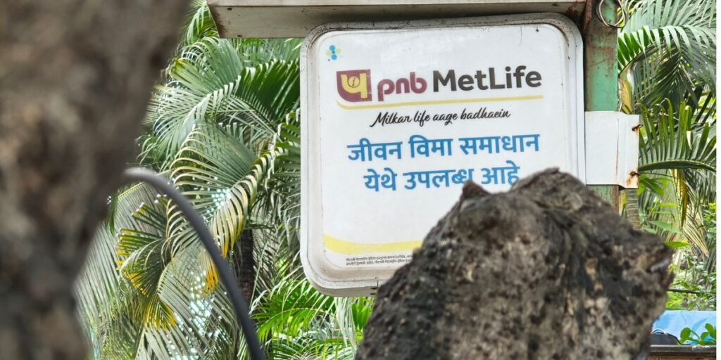 Signboard with the MetLife logo among tropical plants, partially obscured by a rock in the foreground.