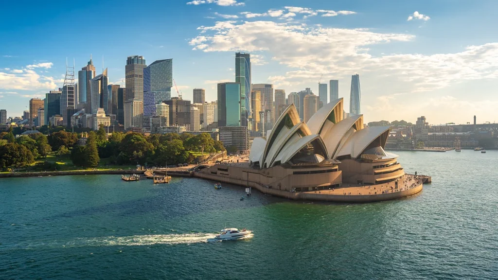 Sydney Opera House by Circular Quay with a city skyline behind on a sunny day.