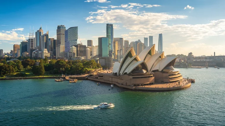 Sydney Opera House by Circular Quay with a city skyline behind on a sunny day.