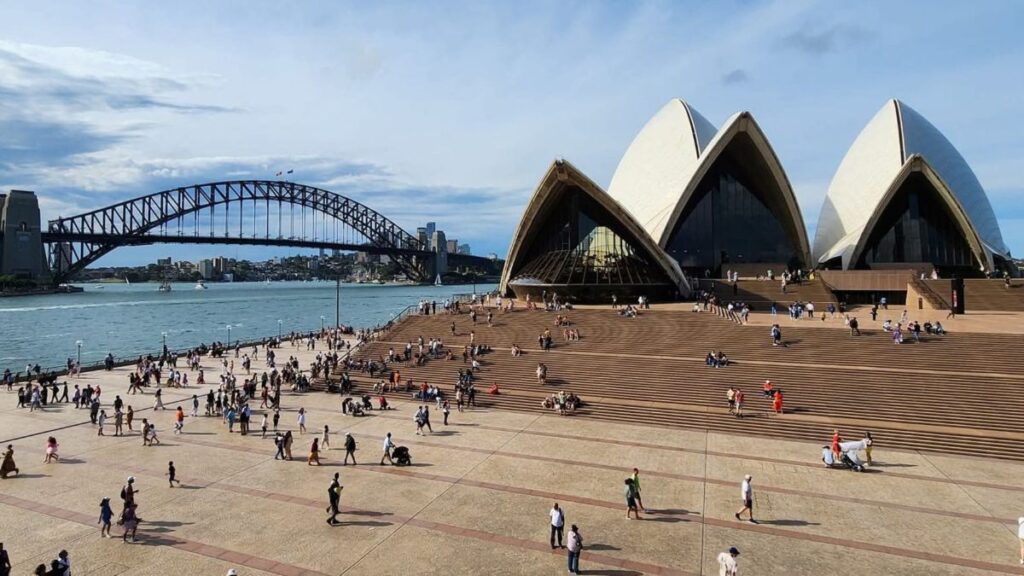 Crowded waterfront at Sydney Harbour with the Opera House foreground and the Harbour Bridge in the distance.
