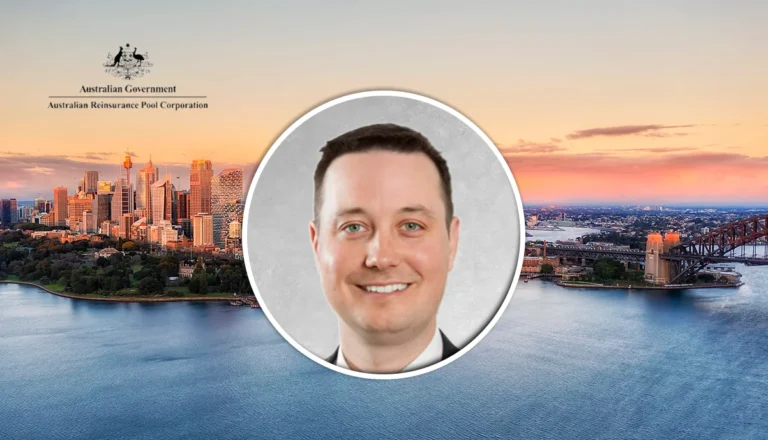 Circular portrait of a smiling man in a suit, over a Sydney harbor sunset with the Australian Government logo in the corner.