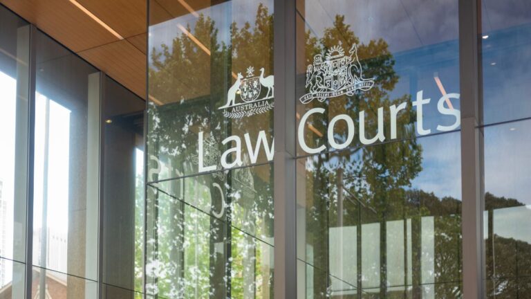 Exterior view of a courthouse entrance with glass panels displaying 'Law Courts' and government crests