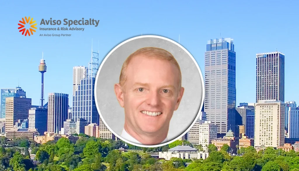 City skyline with tall buildings and a round portrait of a smiling man in the center; Aviso Specialty Insurance & Risk Advisory logo in the top-left corner.
