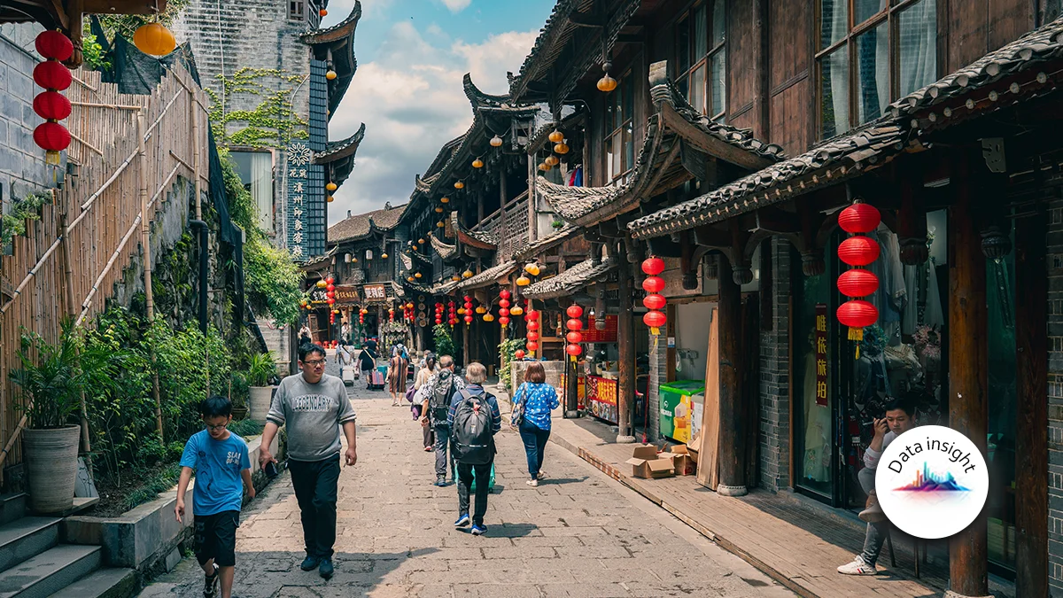 Bustling pedestrian street in a historic Chinese town, with red lanterns hanging between wooden shops.