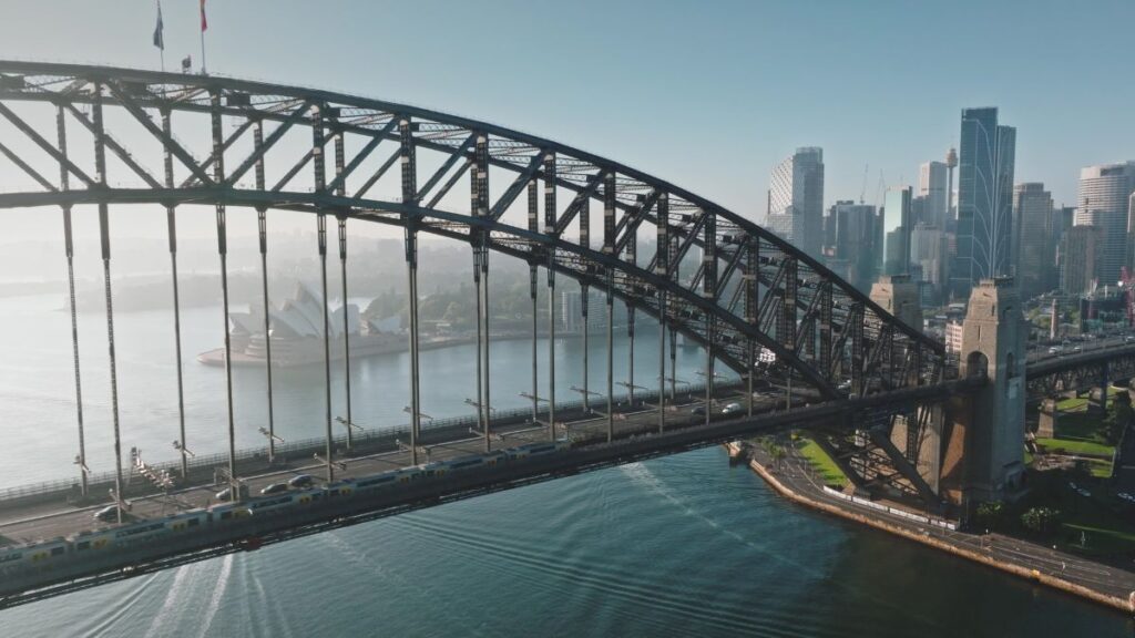 Sydney Harbour Bridge arching over blue water with the Opera House and city skyline in the distance