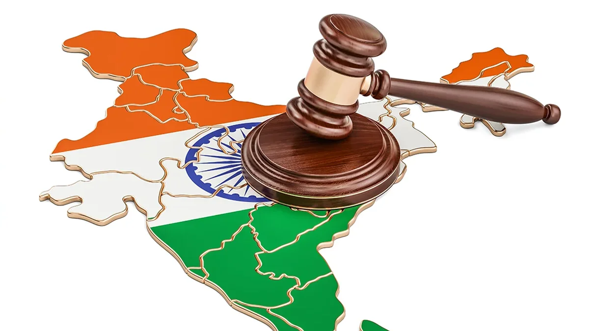 Judicial gavel resting on a stylized map of India highlighted in saffron, white, and green with the blue wheel visible in the center.