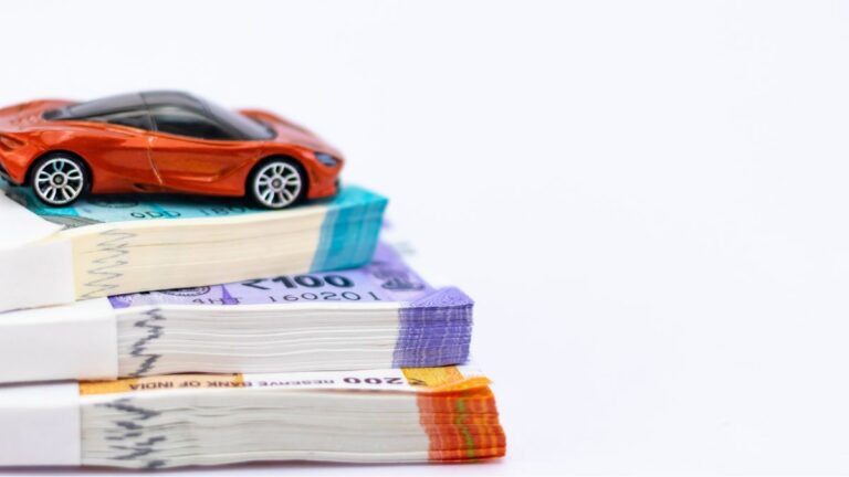 Red toy car perched on top of stacked banknotes, illustrating auto financing or car costs.