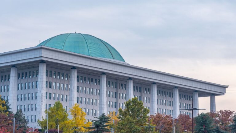 Government-style building with a turquoise dome and tall columns, autumn trees in the foreground.