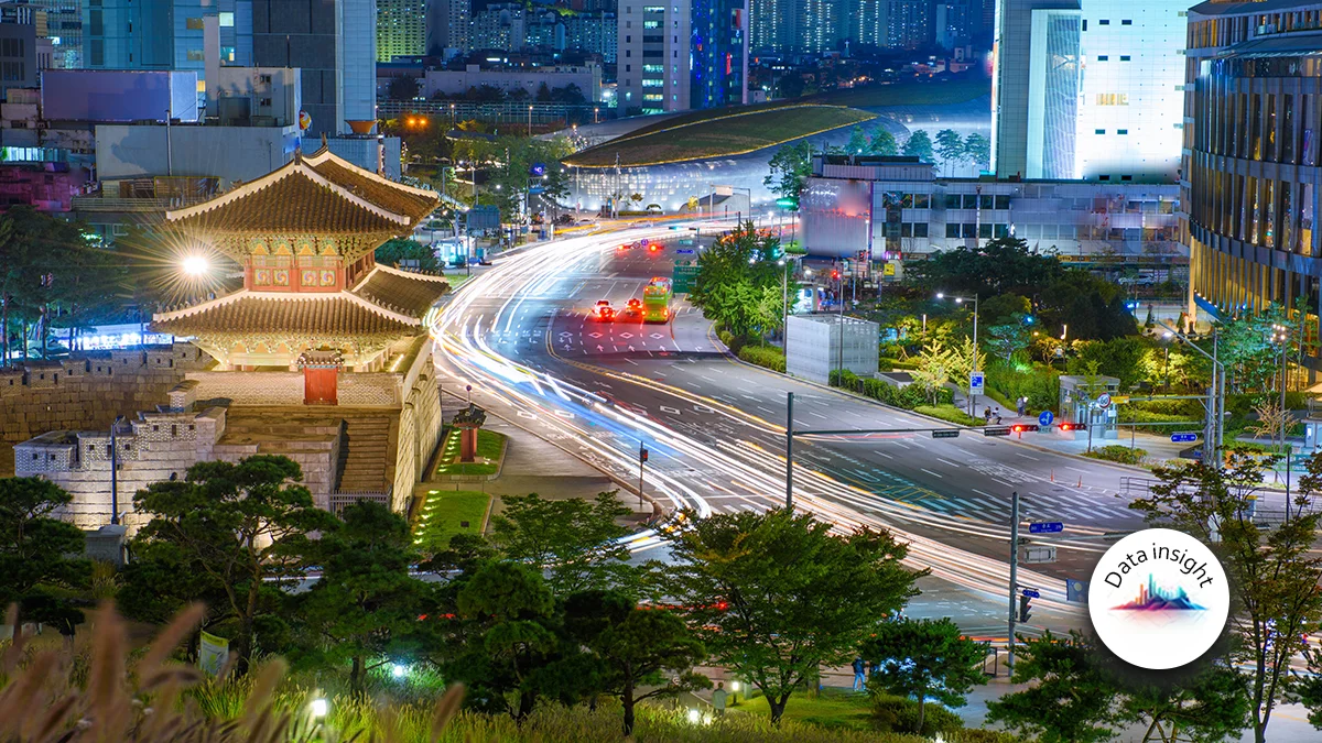 Night cityscape with a traditional pagoda gate beside a curved road and light-trail traffic; modern buildings in the background, Data Insight logo bottom-right.