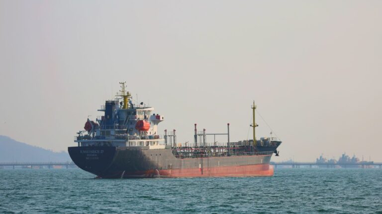 Large cargo tanker sailing on calm sea with a distant industrial shoreline on the horizon
