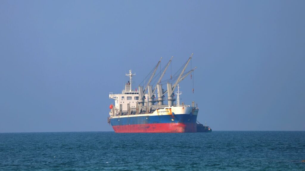 Cargo ship with four gantry cranes on a calm blue sea under a clear sky