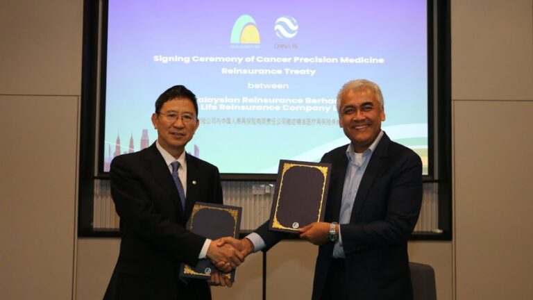 Two men in suits shake hands while holding certificates at a signing ceremony backdrop about a cancer precision medicine reinsurance treaty.