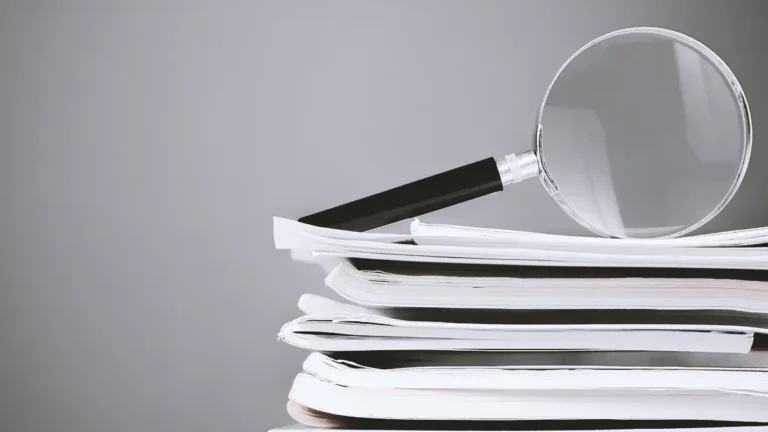 Magnifying glass resting on a stack of papers, suggesting examination or research of documents.