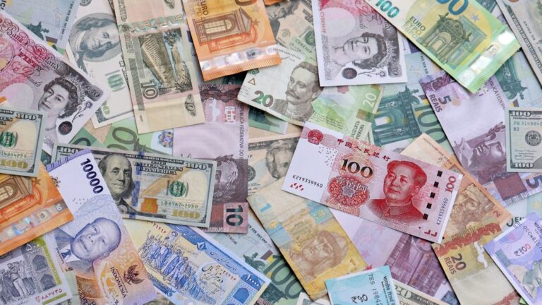 Pile of assorted international banknotes overlapping on a surface, including dollars, euros, yuan and more currencies.