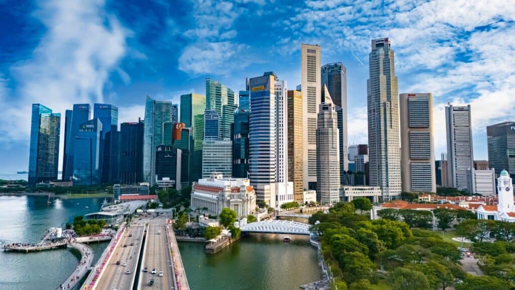 Singapore skyline with tall glass skyscrapers along Marina Bay and a small riverfront park area in the foreground for a cityscape view.