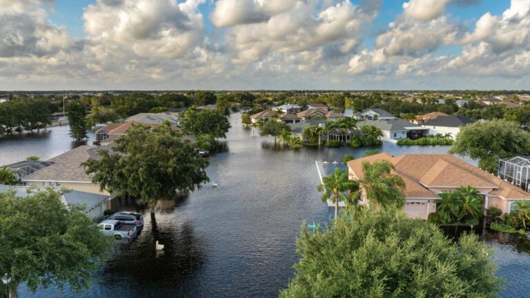 Aerial view of a suburban neighborhood flooded, with water covering streets and yards around houses and trees rising above the water line.