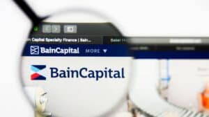 Close-up of a computer screen displaying the Bain Capital logo, viewed through a magnifying glass for emphasis on branding.