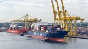 Large container ship CMA CGM loaded with colorful stacked cargo at a busy port with tall yellow gantry cranes nearby