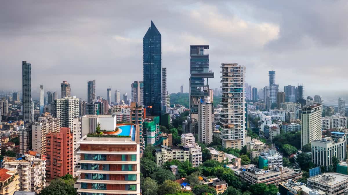 Panoramic city skyline with tall glass skyscraper and apartment blocks, a rooftop pool in the foreground, and an overcast sky.