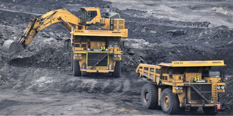 Two large yellow mining machines—an excavator loading material into a dump truck at a coal/open-pit mine site.