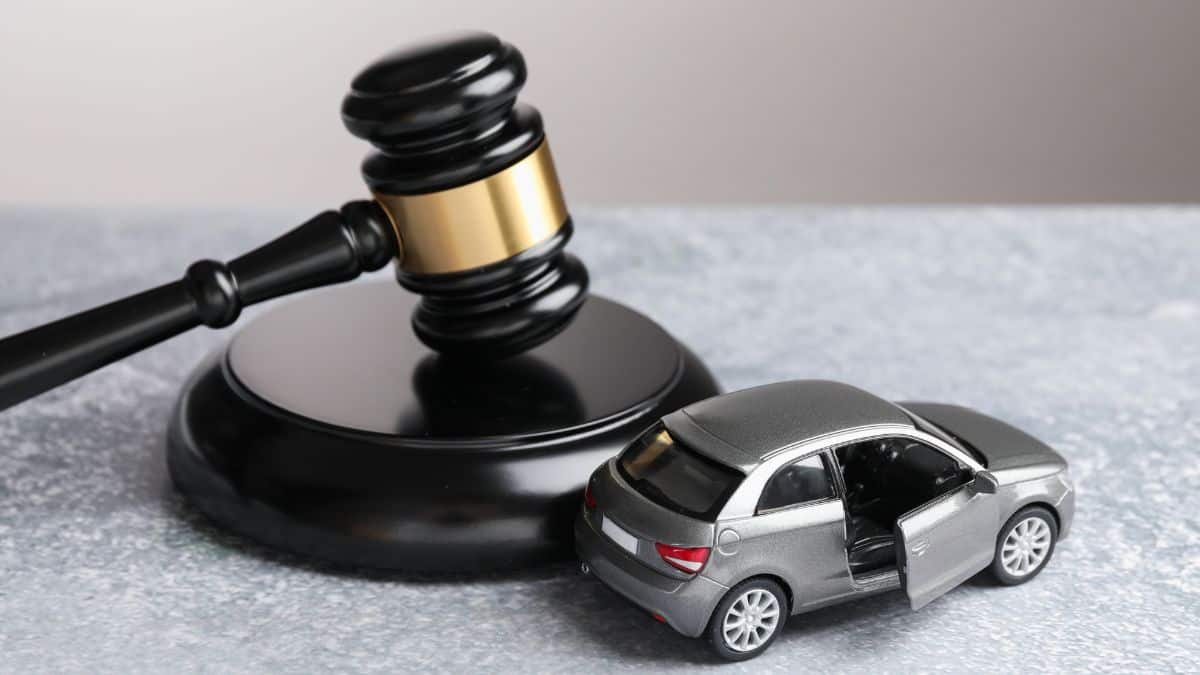 Gavel beside a silver toy car with an open door on a gray surface, suggesting auto law or car accident legal matters.