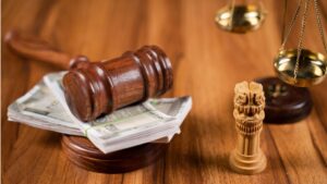LIC faces US$11.4m GST exposure over FY2022-23 input tax credit claims Judge's gavel resting on a stack of cash with a scales of justice in the background, on a wooden table.